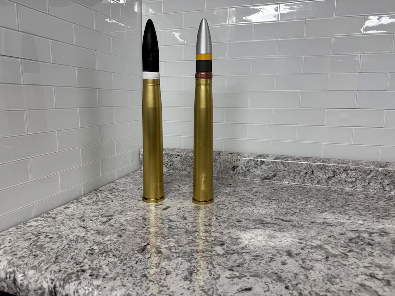 May include: Two gold-coloured artillery shells, one with a black tip and the other with a silver tip and yellow and brown bands.