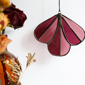 May include: A stained glass window hanging ornament in the shape of a flower with pink and burgundy glass panels.