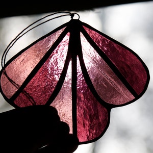 May include: A pink stained glass ornament shaped like a flower with a black string for hanging.