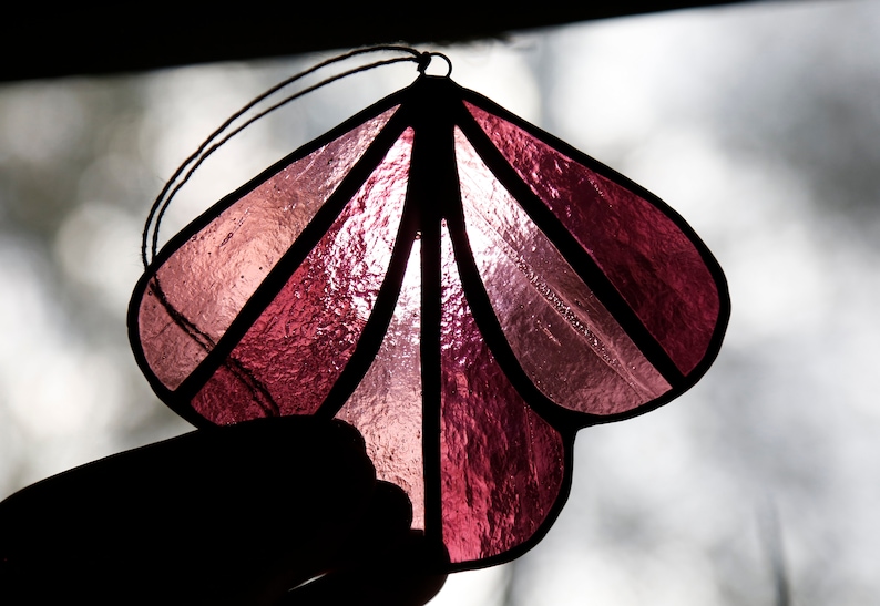 May include: A pink stained glass ornament shaped like a flower with a black string for hanging.