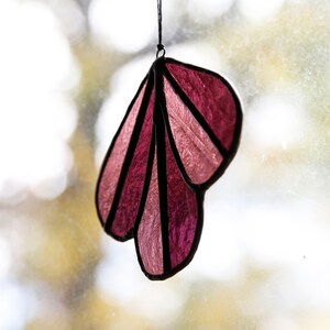 May include: A pink and purple stained glass suncatcher shaped like a leaf, hanging from a window.