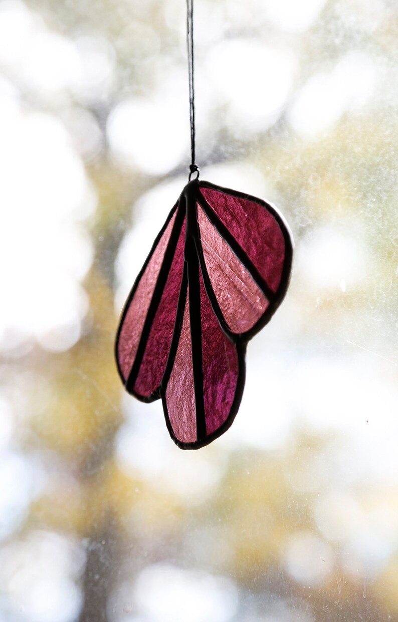 May include: A pink and purple stained glass suncatcher shaped like a leaf, hanging from a window.