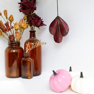 May include: Three brown glass bottles with dried flowers and a stained glass leaf hanging from the ceiling. Two small pumpkins, one pink and one white, are in the foreground.