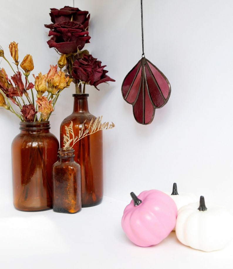 May include: Three brown glass bottles with dried flowers and a stained glass leaf hanging from the ceiling. Two small pumpkins, one pink and one white, are in the foreground.