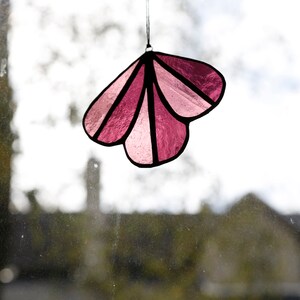 May include: A pink stained glass suncatcher shaped like a flower with five petals. The suncatcher is hanging from a string.