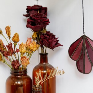 May include: Two brown glass vases with dried flowers. One vase holds dried red roses and the other holds dried yellow and orange flowers. A stained glass hanging in the shape of a leaf with shades of pink and red hangs from the ceiling.