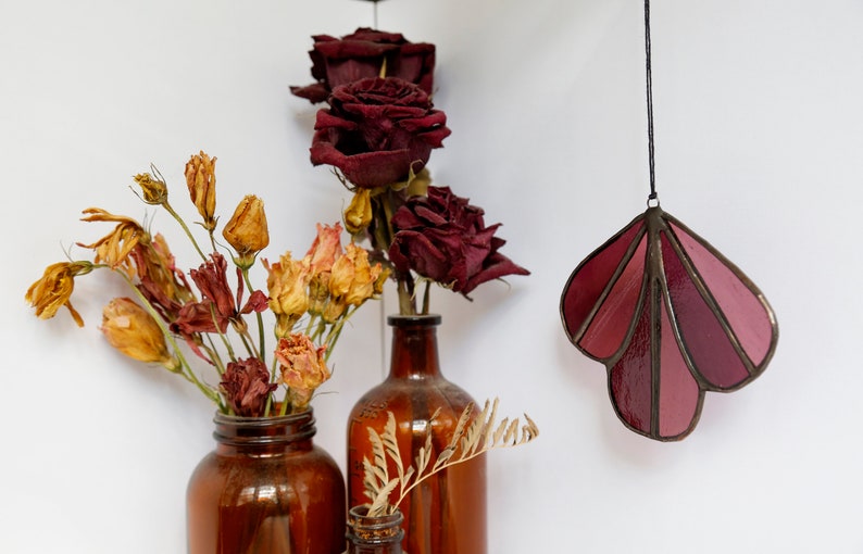 May include: Two brown glass vases with dried flowers. One vase holds dried red roses and the other holds dried yellow and orange flowers. A stained glass hanging in the shape of a leaf with shades of pink and red hangs from the ceiling.