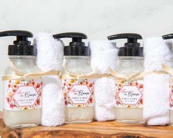 May include: Four clear glass bottles with black pump tops and white labels. The labels have a floral design and the text "Love in Bloom" with the names "Emily & Mike". Each bottle is wrapped with a white hand towel.