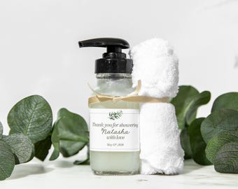 May include: A small clear bottle with a black pump dispenser and a white hand towel tied around the neck. The bottle has a label that says "Thank you for showering Natasha with love May 17th, 2020".