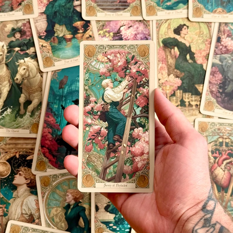 Op de afbeelding: Een rechthoekige tarotkaart getiteld Scorn of Pleiades met een illustratie van een persoon in een donkergroene tuinbroek die een houten ladder beklimt om roze bloemen in een kas te bereiken, omlijst door een sierlijke gouden rand.