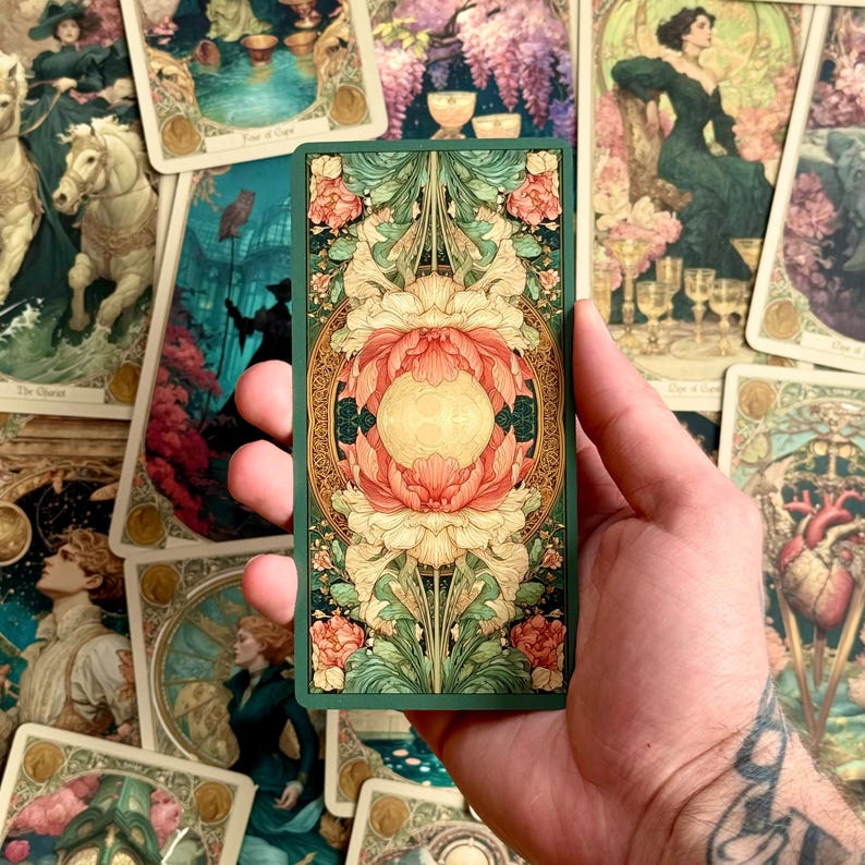Op de afbeelding: Een rechthoekige tarotkaart met een symmetrisch, sierlijk ontwerp met een centrale gouden cirkel omringd door gelaagde, gestileerde koraalroze en cr&egrave;mekleurige bloemmotieven, alles tegen een diepgroene achtergrond met ingewikkeld goud filigraan.