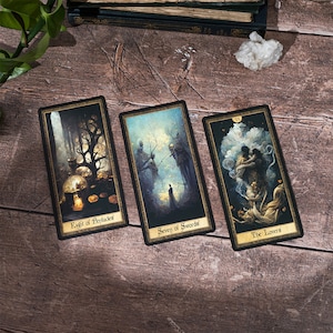 May include: Three tarot cards on a wooden surface. The cards are "Eight of Pentacles", "Seven of Swords", and "The Lovers". The cards are illustrated with dark, moody imagery.
