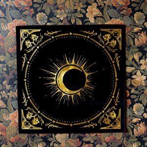 May include: A black velvet square with a gold sun and crescent moon design. The design is surrounded by a decorative border.