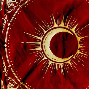 May include: A red fabric tapestry with a gold crescent moon and sun design. The moon is inside the sun, which has rays radiating out from it.