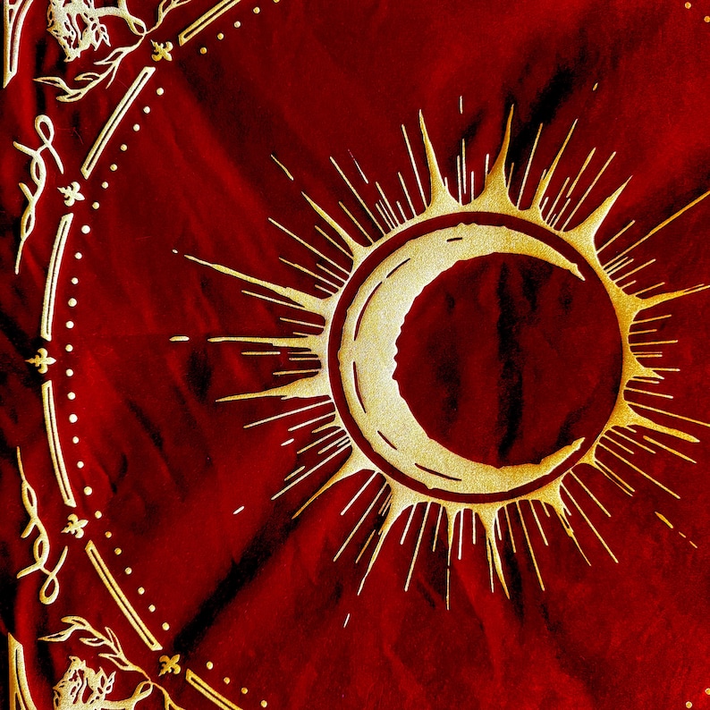 May include: A red fabric tapestry with a gold crescent moon and sun design. The moon is inside the sun, which has rays radiating out from it.