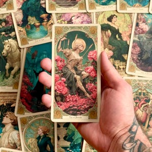 Op de afbeelding: Een rechthoekige tarotkaart getiteld Ten of Swords met een illustratie van een figuur met zwaarden door de rug, omringd door roze rozen en een gouden halo, tegen een donkergroene achtergrond met een sierlijke decoratieve rand.
