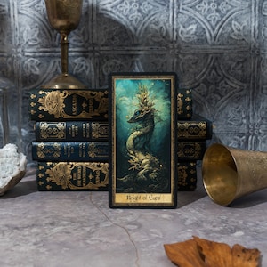 May include: A tarot card with a dark blue and green background featuring a gold and green creature with a crown of leaves. The card is titled "Knight of Cups".