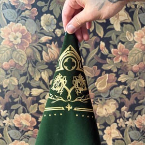 May include: A green velvet fabric with gold embroidery. The design features a quatrefoil, two stylized trees, and a fleur-de-lis.