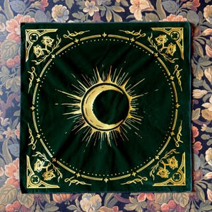 May include: A green velvet bandana with a gold crescent moon and sun design. The bandana has a gold border with a repeating floral pattern.