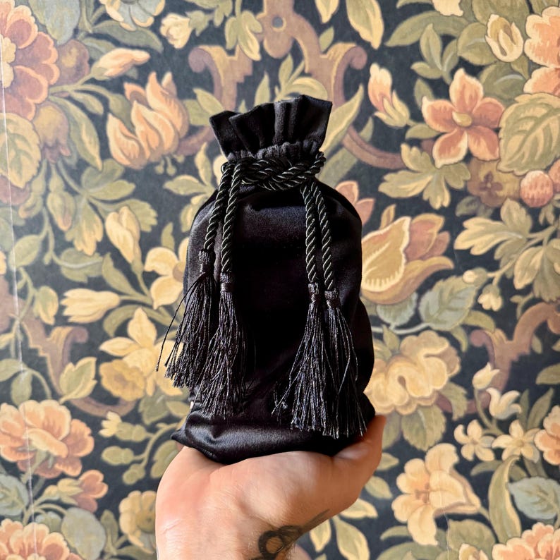 May include: A black velvet drawstring bag with black tassels. The bag is held in a hand.