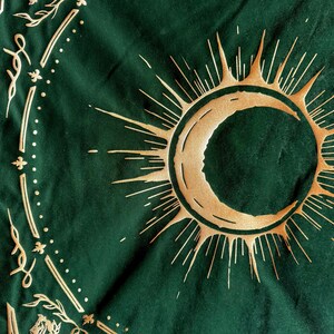 May include: A green tapestry with a gold crescent moon and sun design. The sun has a radiating pattern of gold lines.