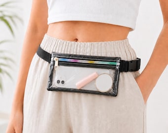 Può includere: Un marsupio rettangolare trasparente con bordo nero e cerniera arcobaleno. Il marsupio contiene uno smartphone, un rossetto e uno specchietto compatto. La cintura nera ha una chiusura a fibbia.