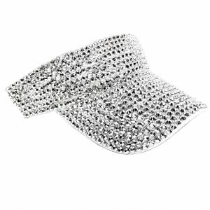 Puede incluir: Una visera plateada cubierta de peque&ntilde;os y brillantes pedrer&iacute;a. La visera es curvada y tiene una ala ancha para dar sombra. La pedrer&iacute;a refleja la luz, creando un efecto deslumbrante. Este accesorio est&aacute; dise&ntilde;ado para ser usado en la cabeza.