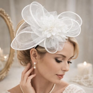May include: A white, floral-shaped headpiece with a sheer, layered design. The headpiece features a central flower with pearl accents and is attached to a thin, black headband. This elegant accessory is suitable for weddings or special occasions.