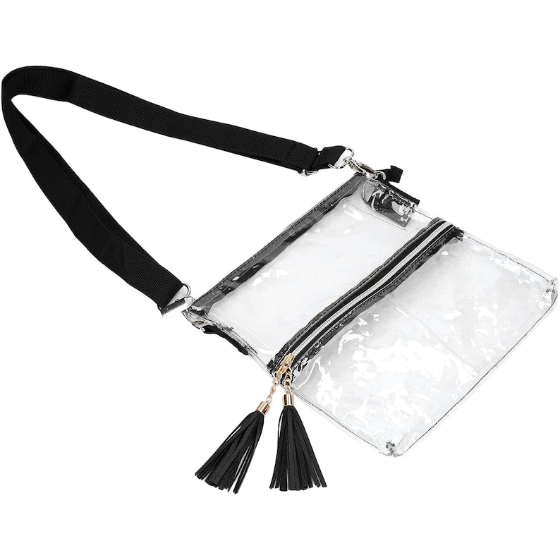 May include: Transparent crossbody bag with a black strap and zip. The bag features a black and white striped zip and two black tassels hanging from the zip pull. The bag is made of clear plastic.