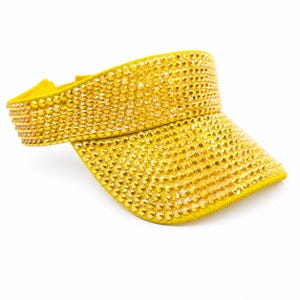 Puede incluir: Visera amarilla cubierta de peque&ntilde;os y brillantes pedrer&iacute;a dorada. La visera tiene una visera curva y una banda el&aacute;stica. El accesorio est&aacute; dise&ntilde;ado para proteger los ojos del sol.