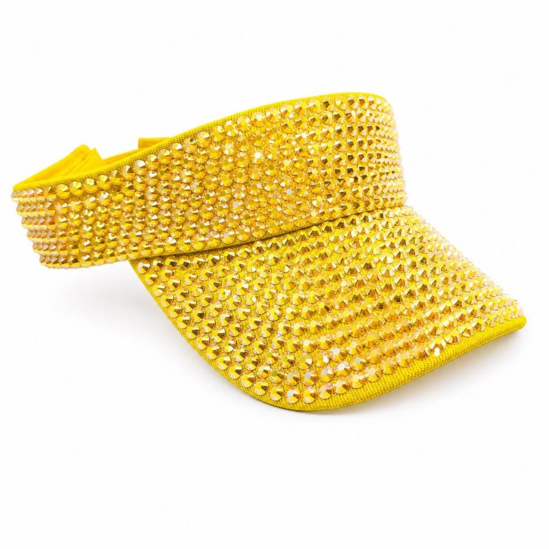 Puede incluir: Visera amarilla cubierta de peque&ntilde;os y brillantes pedrer&iacute;a dorada. La visera tiene una visera curva y una banda el&aacute;stica. El accesorio est&aacute; dise&ntilde;ado para proteger los ojos del sol.