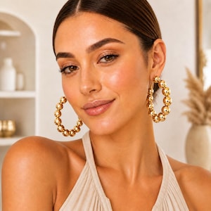 May include: Gold-colored hoop earrings with a beaded design. The earrings are made of small, round beads that are strung together to form a circular shape. The earrings are worn on the ear.