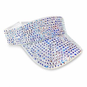 Puede incluir: Una visera blanca cubierta de pedrer&iacute;a iridiscente. La visera tiene una visera curva y una banda el&aacute;stica blanca. La pedrer&iacute;a refleja una variedad de colores, incluyendo azul, morado y plateado. La visera est&aacute; dise&ntilde;ada para proteger los ojos del sol.