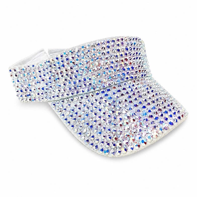 Puede incluir: Una visera blanca cubierta de pedrer&iacute;a iridiscente. La visera tiene una visera curva y una banda el&aacute;stica blanca. La pedrer&iacute;a refleja una variedad de colores, incluyendo azul, morado y plateado. La visera est&aacute; dise&ntilde;ada para proteger los ojos del sol.