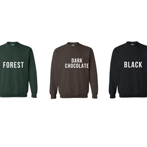 May include: Three crewneck sweatshirts in different colors: forest green, dark chocolate brown, and black. Each sweatshirt has a white text design on the front. The green sweatshirt says "FOREST", the brown sweatshirt says "DARK CHOCOLATE", and the black sweatshirt says "BLACK".