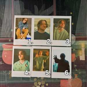 May include: A collection of six Polaroid-style photographs featuring a man in various poses and outfits. The photos showcase the man in different settings, wearing casual clothing, with varying facial expressions. The images are arranged on a patterned surface.