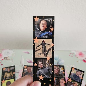 May include: A black bookmark featuring three film strip style images of a person. The bookmark is decorated with orange star and flower stickers. Other bookmarks with similar images are visible.