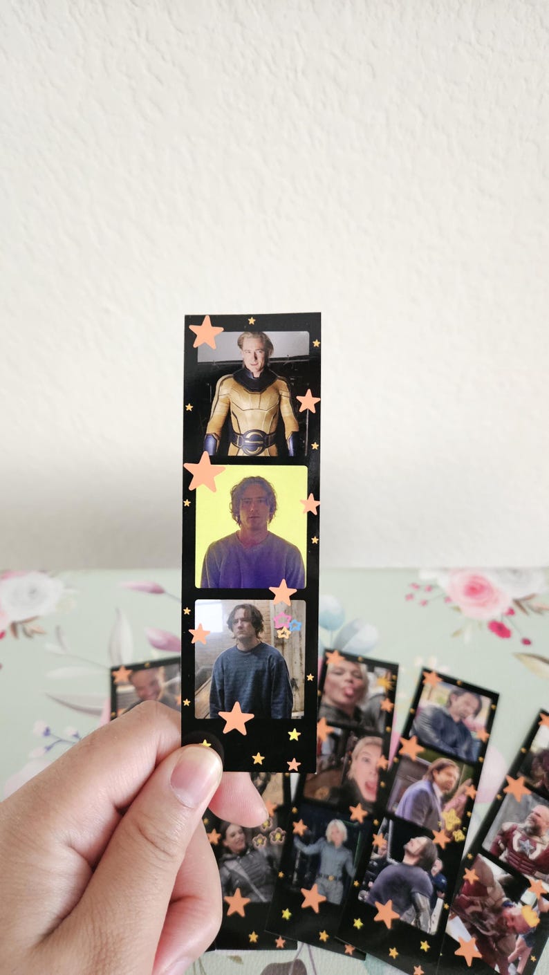 May include: Black film strip bookmark with three images of a person, decorated with orange star stickers. The bookmark is held in a hand. Other similar bookmarks are visible in the background.