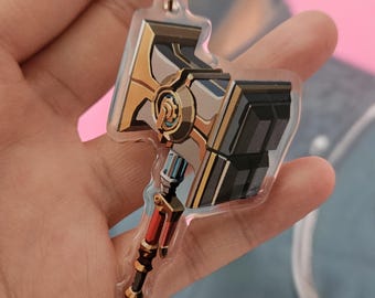 Könnte beinhalten: Ein Schlüsselanhänger aus klarem Acryl mit einer detaillierten Illustration eines mechanischen Hammers. Der Hammer hat einen gold-grauen Kopf mit schwarzen Akzenten, einen blau-silbernen Zahnradmechanismus und einen rot-schwarzen Griff.