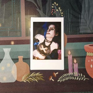 May include: A Polaroid photograph of a woman with blue hair wearing a brown leather top with a cross design. The photo is framed in a white border and is sitting on a table with a dark brown surface.