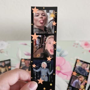 May include: A black film strip with three images of a person, decorated with orange star cutouts. The images show the person making faces and posing. The film strip is held by a hand.