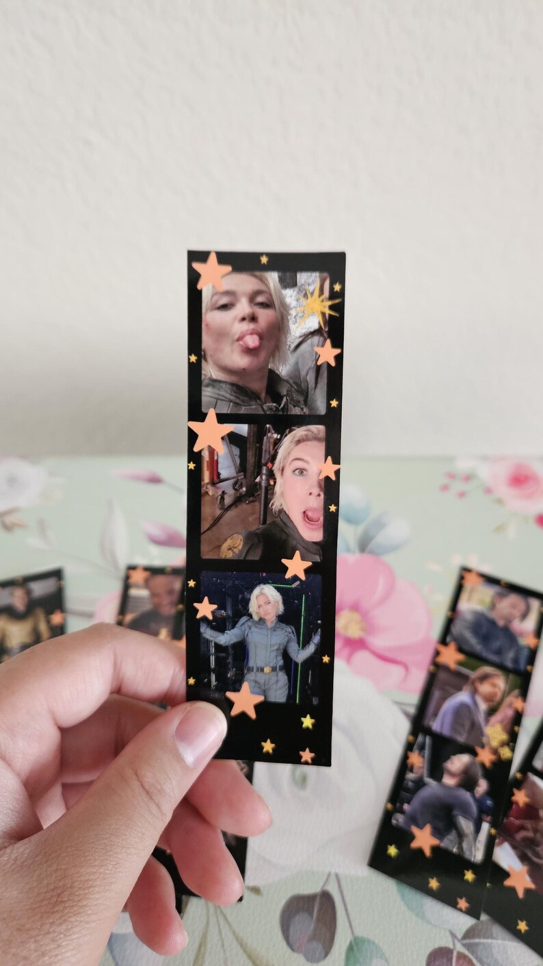 May include: A black film strip with three images of a person, decorated with orange star cutouts. The images show the person making faces and posing. The film strip is held by a hand.
