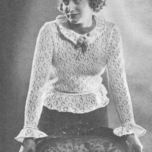 Puede incluir: Fotografía en blanco y negro de una mujer con un suéter blanco de punto calado. El suéter tiene un cuello con volantes, mangas largas con puños acampanados y una cintura peplum. La mujer está sentada.