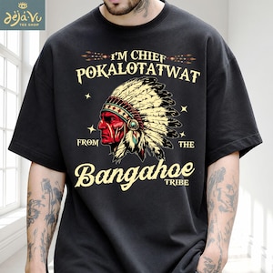 May include: A black short-sleeve t-shirt featuring a graphic of a person wearing a feathered headdress. The text reads I'M CHIEF POKALOTATWAT FROM THE Bangahoe TRIBE. The design includes cream-colored lettering and a detailed illustration of the figure.