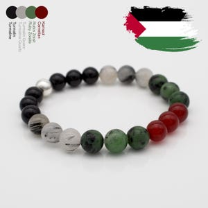 Könnte beinhalten: Ein Armband aus schwarzen, grauen, grünen und roten Perlen mit einem silbernen Anhänger. Die Perlen bestehen aus verschiedenen Edelsteinen, darunter schwarzer Turmalin, grauer Quarz, grüner Zoisit und roter Karneol.