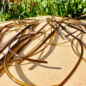 May include: A close-up of a pile of brown glass rods, some of which are bent into curved shapes. The rods are lying on a light brown surface.