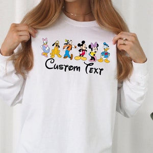 May include: White long-sleeve shirt with a graphic of Mickey Mouse and friends. The text "Custom Text" is printed below the graphic.