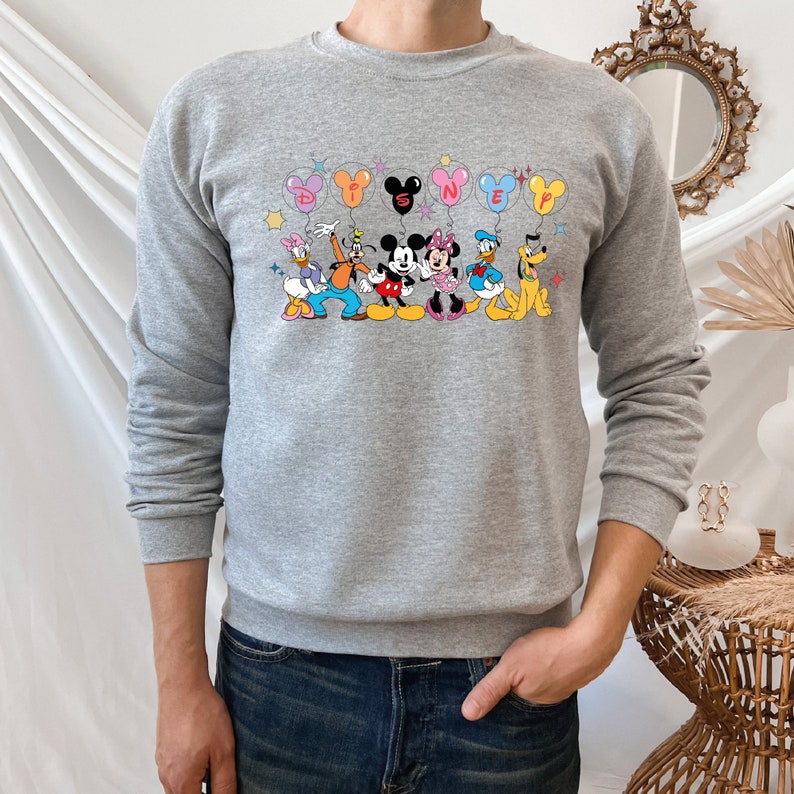 May include: A gray sweatshirt with a print of Mickey Mouse and his friends holding balloons that spell out "DISNEY".