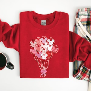 May include: Red sweatshirt with a design of pink, red, and white Mickey Mouse heads shaped like balloons. The balloons are tied together with a pink ribbon.