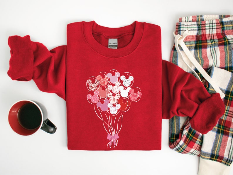 May include: Red sweatshirt with a design of pink, red, and white Mickey Mouse heads shaped like balloons. The balloons are tied together with a pink ribbon.